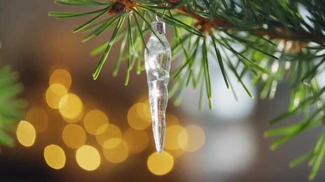 Close up of a single icicle hanging from a pine tree branch with bokeh lights in the background.