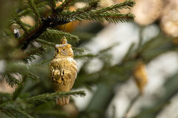 Golden owl Christmas ornament hanging on evergreen tree branch holiday decor