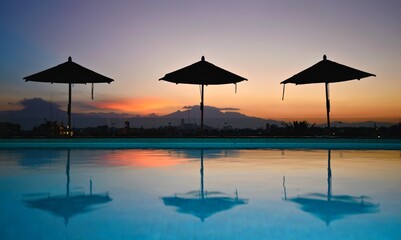 Landscape with scenic sunset pool view and parasol silhouettes as seen from the Rosewood Hotel roof garden terrace in Puebla, Mexico. 