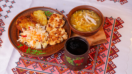 Traditional Ukrainian lunch with chicken noodle soup, potato pancakes and meat on embroidered tablecloth
