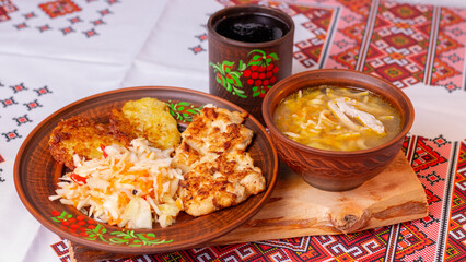 Traditional Ukrainian lunch with chicken noodle soup, potato pancakes and meat on embroidered tablecloth