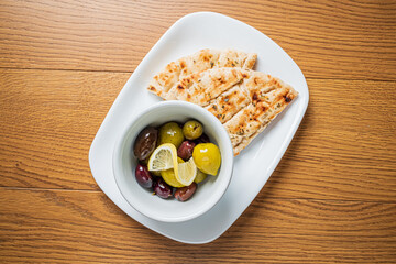 Grilled flatbread sits by a bowl of olives and vibrant lemon wedges, inviting a taste
