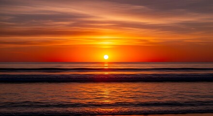Obraz premium Vibrant orange sunset over calm ocean waves with golden light reflection