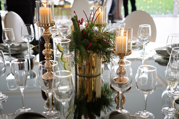 A festive dining table decorated with candles, glassware, and a centerpiece of greenery and berries in a reflective setting