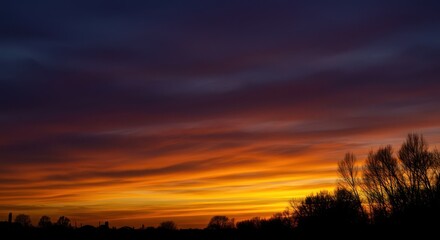 Obraz premium Dramatic evening sky with vibrant orange, yellow, and purple colors. Dark foreground creating a stark silhouette contrast, vibrant, peaceful, dramatic
