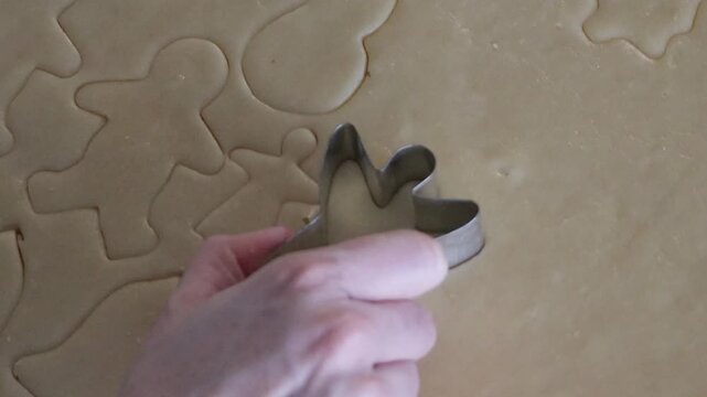 An extreme close up of an angel shaped cookie cutter being used to cut out a cookie in a sheet of holiday shaped cookies.