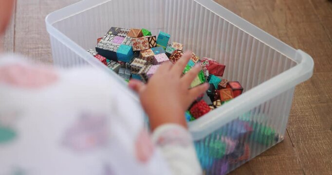 Close up of young boy hand cleaning up toy blocks and putting them into a clear plastic storage container on wooden floor. Childhood organization and tidiness concept. High quality 4K video.