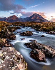 A fast-flowing stream cascades through rocky terrain towards distant, imposing mountains under a vibrant, cloud-filled sky