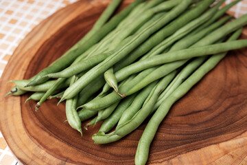 Freshly green beans arranged on a wooden cutting board create an appealing display against a table background, perfect for highlighting healthy eating