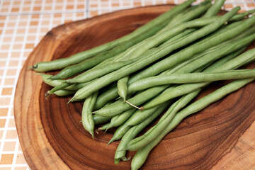 Freshly green beans arranged on a wooden cutting board create an appealing display against a table background, perfect for highlighting healthy eating
