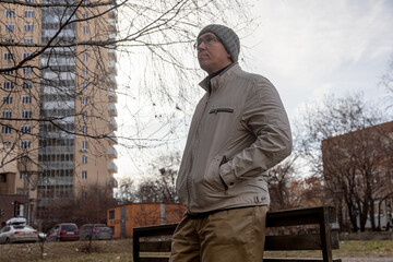 Fototapeta premium Man standing in a city park waiting for a meeting during the autumn season. Casual urban outdoor scene with adult male.