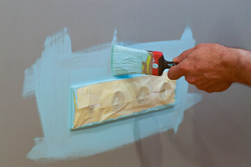 Home interior update involving painting around an electrical outlet with a brush, employing masking tape for protection, as part of a DIY project to maintain a tidy and safe space.