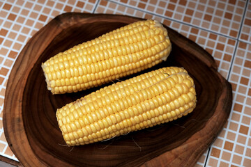 Fresh raw yellow ​​sweet corn on a wooden chopping board. healthy traditional snack, suitable for themes like healthy eating, summer produce, agriculture, vegan food, and natural lifestyle.