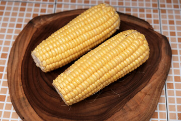 Fresh raw yellow ​​sweet corn on a wooden chopping board. healthy traditional snack, suitable for themes like healthy eating, summer produce, agriculture, vegan food, and natural lifestyle.