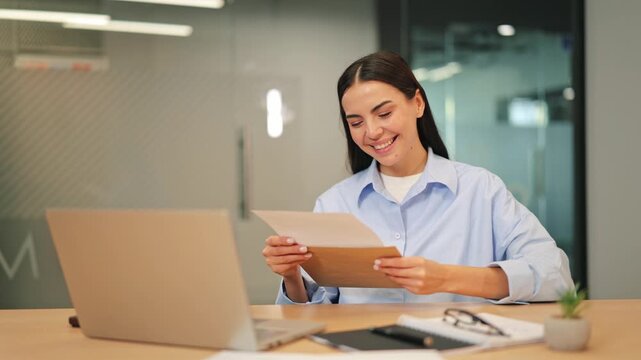 Woman in modern office smiles brightly, reading good news in letter. Expresses joy, excitement, and positive emotion. Achieves success in business, feeling confident and satisfied with outcome.
