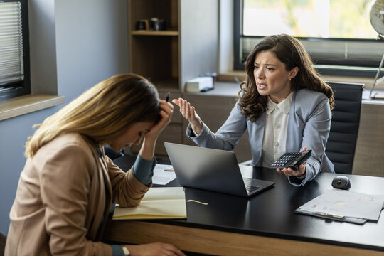 Two businesswomen engage in a tense discussion during a financial meeting in a modern office space