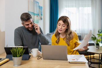 Man and woman collaborate on a project at a bright home office while using technology and discussing on the phone