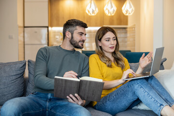 Couple working together on a laptop while discussing ideas in a cozy living room