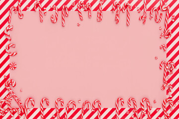 Festive holiday border with red and white candy canes and peppermints on a pink background. Perfect for sweet seasonal greetings. copy space
