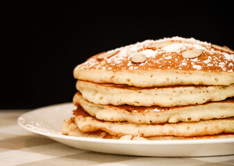 A stack of five golden brown pancakes with powdered sugar and almonds.