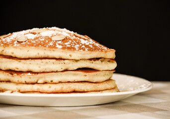 A stack of five golden brown pancakes with powdered sugar and almonds.