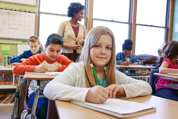 Learning, portrait and writing with girl in school classroom for development, future or growth. Book, education and study with cute child student at desk in class for knowledge, lecture or lesson