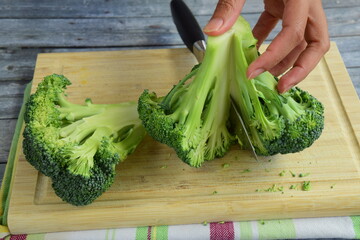 cutting fresh broccoli with knife on wooden board