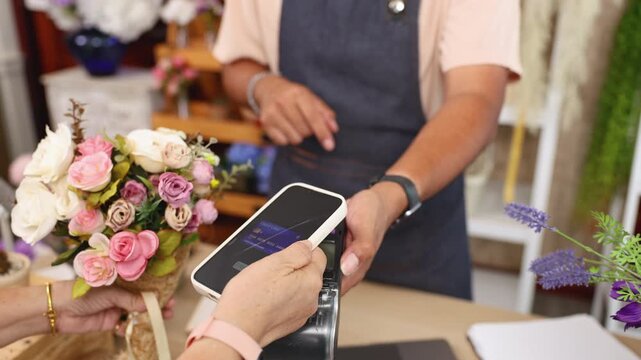 Small business flower owner shop handles payment credit card purchase transaction, Asian florist hand holding bouquet while paying, modern retail store using cashless system for customer convenience