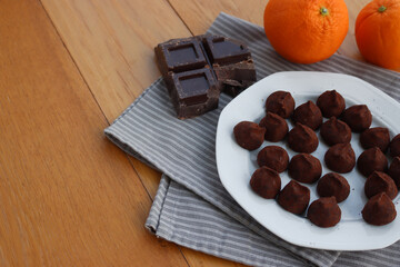 Dark Chocolate truffles candies with candied orange pells on white ceramic plate on wooden table with copy space