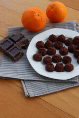 Dark Chocolate truffles candies with candied orange pells on white ceramic plate on wooden table with copy space