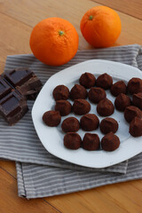 Dark Chocolate truffles candies with candied orange pells on white ceramic plate on wooden table