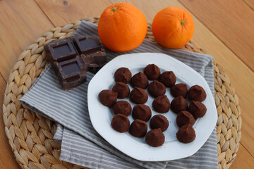 Dark Chocolate truffles candies with candied orange pells on white ceramic plate on wooden table