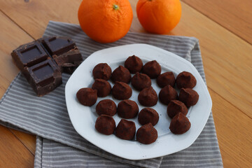 Dark Chocolate truffles candies with candied orange pells on white ceramic plate on wooden table