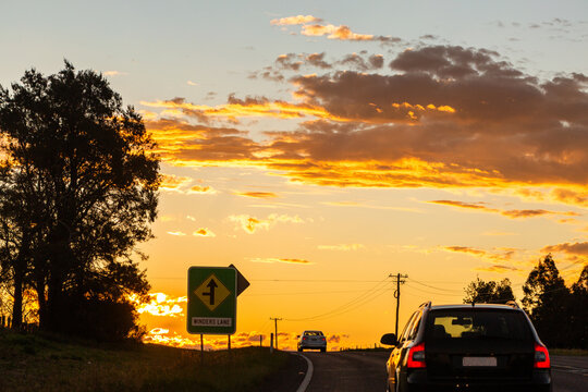 cars traveling on road towards crest at the end of the day with sunset sky