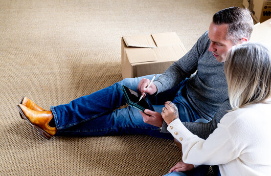 Man sitting on the carpeted floor holding a tablet and stylus with wife beside him