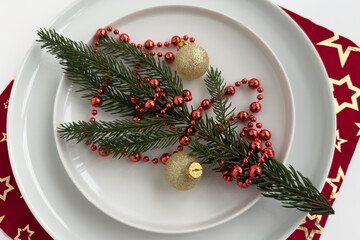 Festive holiday table setting featuring evergreen branches, red beads, and golden ornaments arranged on a white plate with a decorative star-patterned napkin