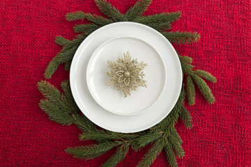 Elegant white plates arranged on a festive red tablecloth, surrounded by evergreen branches, showcasing a beautiful holiday dining setup with decorative snowflake centerpiece