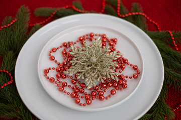 Decorative holiday plate featuring a golden floral ornament surrounded by red beads and green pine branches, creating a festive and elegant table setting for celebrations