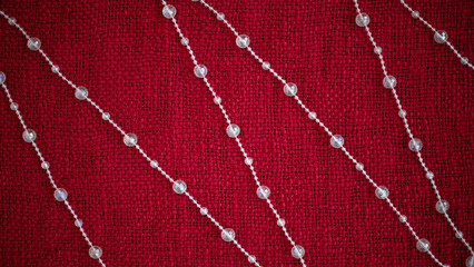 Elegant strands of clear beads arranged in a diagonal pattern on a rich red textured fabric background, showcasing intricate design and festive ambiance for decoration