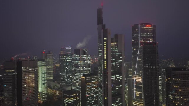 Aerial view of Frankfurt's financial district at night. Glowing office buildings like Commerzbank Tower and Trianon and skyscrapers of multinational corporations