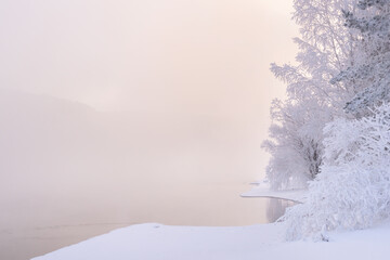 The magical winter background of copy space is a frosty January winter morning on the river, tree...
