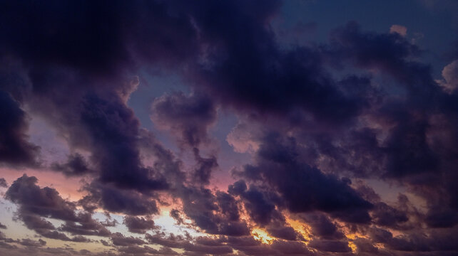Dramatic dark storm clouds gather over a tranquil beach at dusk, reflecting soft golden light onto the crashing ocean waves
