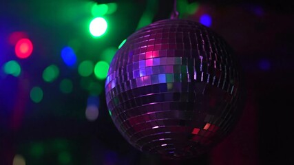 Close-up of a disco ball reflecting vibrant lights. Green, red, and blue orbs blur in the background