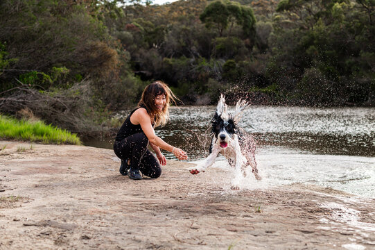 A woman joyfully interacts with her dog, splashing in the river on a warm day