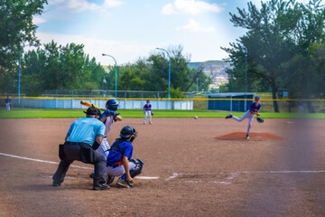 Young baseball pitcher throwing ball during game with batter, catcher and umpire watching