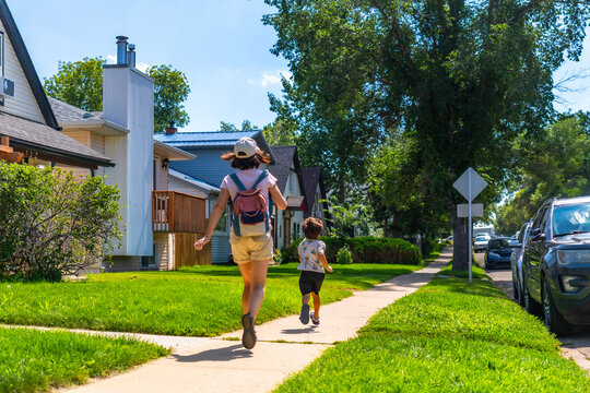 Mother and son running on sidewalk in suburban neighborhood of drumheller, canada