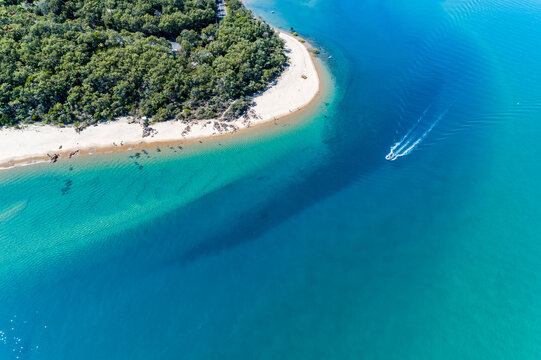 Speed boat passing sandy beach and point on a tidal creek at Seventeen Seventy, Queensland