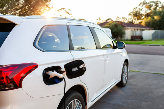 hybrid car charger plugged into vehicle parked in home driveway at sunset