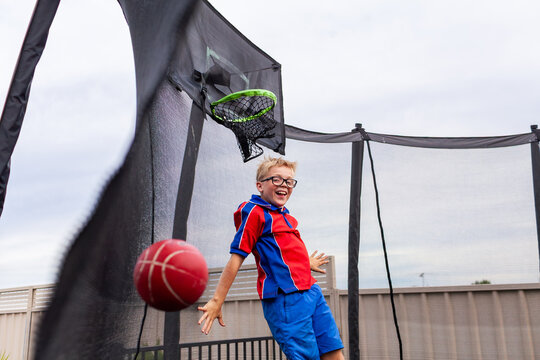 Boy bouncing on trampoline playing ball game on overcast day after school