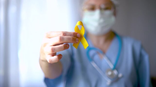 A nurse or doctor in medical attire holds a yellow ribbon representing bone diseases, childhood cancer, suicide prevention, and liver disease awareness.
